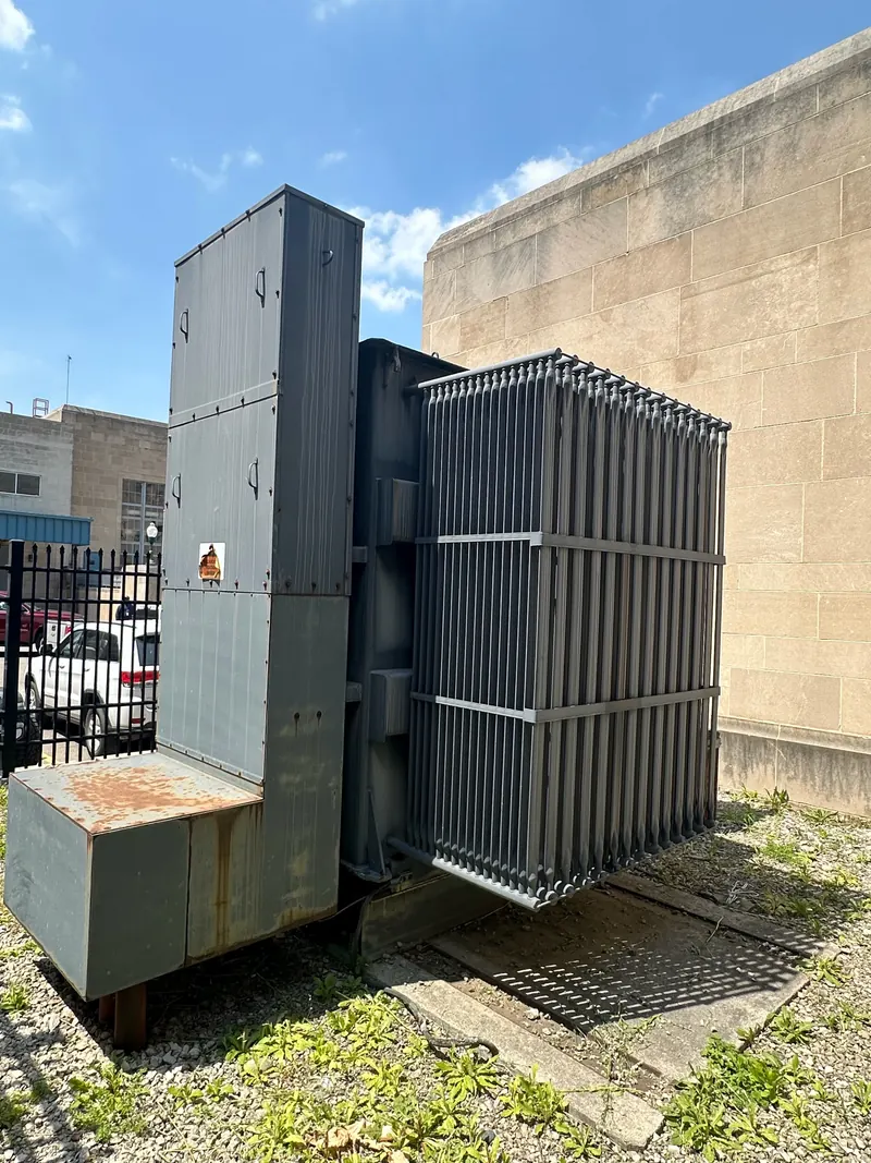 Large industrial liquid-filled transformer with external radiator banks beside a commercial building