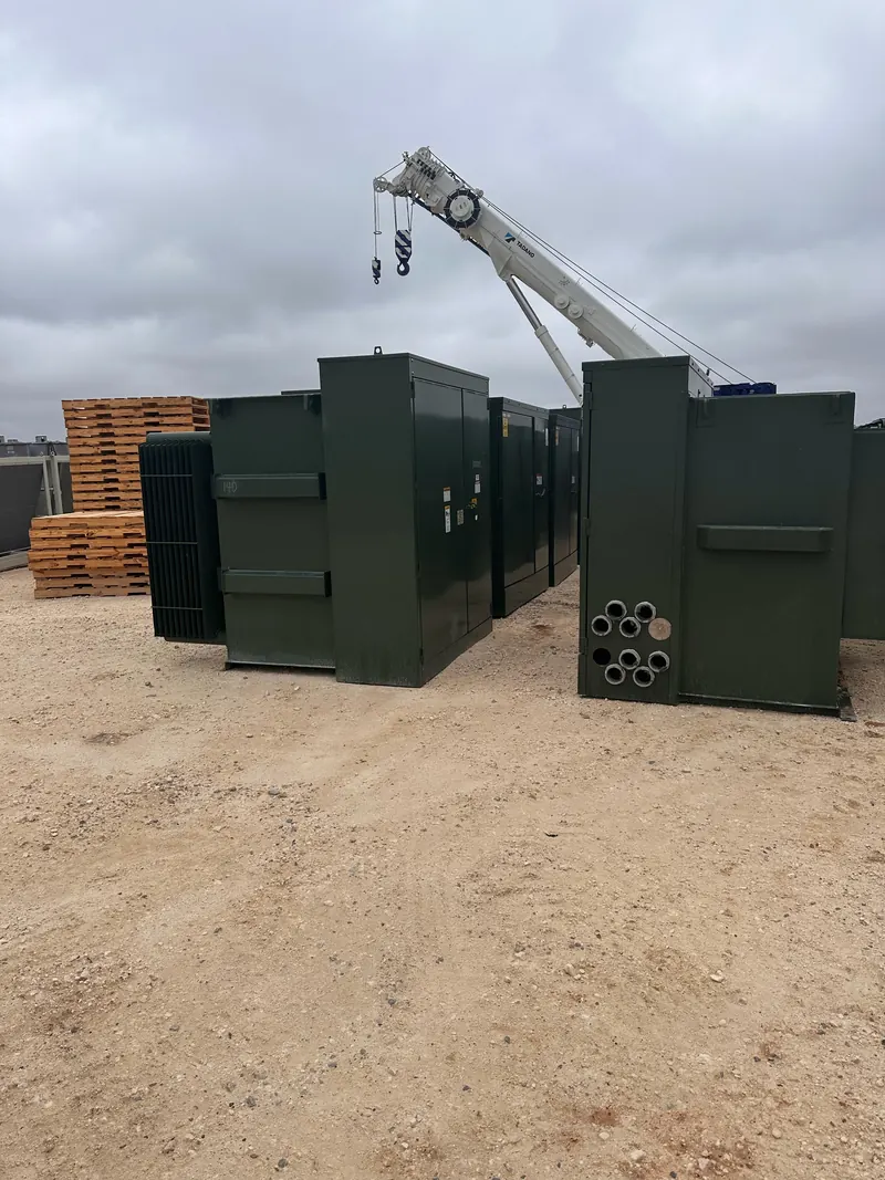 Several green pad-mounted transformers staged outdoors with a mobile crane in the background