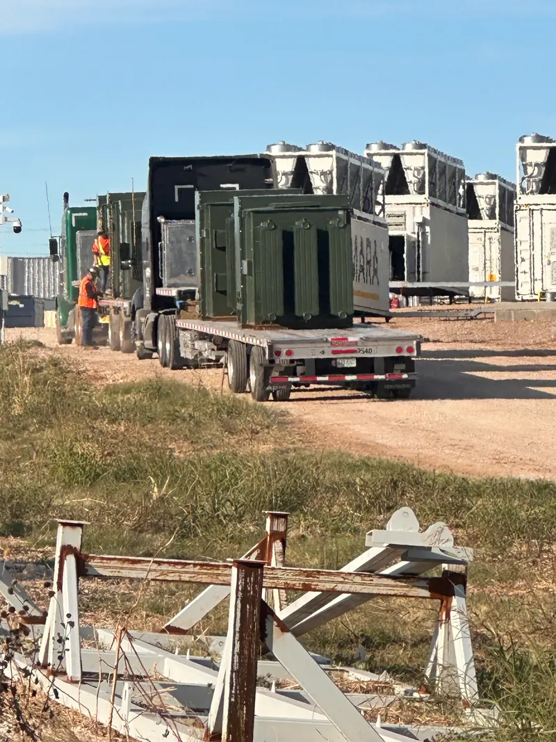 Electrical transformer on a flatbed truck at an industrial project site with workers nearby
