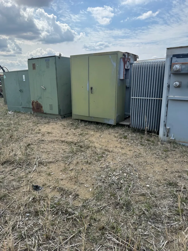Used electrical transformers and enclosures stored outdoors in varied condition